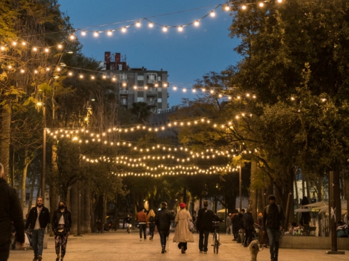 Image of a brick street lined with trees, people walking, and string lights in zig zag pattern above.